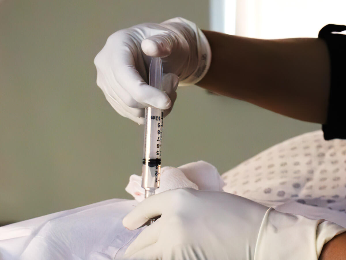 Regenerative Injection Therapy Gloved clinician holding a syringe while administering an image-guided injection into a patient’s knee during orthopaedic pain-management treatment.