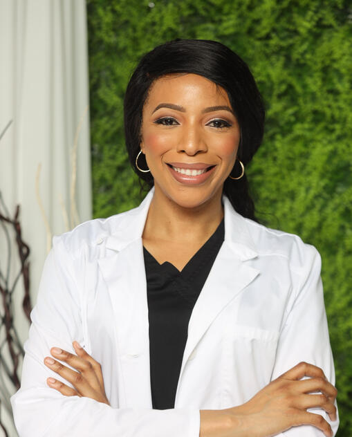 Dr. Kessiena Aya – Orthopedic Spine and Pain Specialist Dr. Kessiena Aya, orthopedic surgeon, standing confidently in a white coat with a professional smile, in front of a green natural backdrop.
